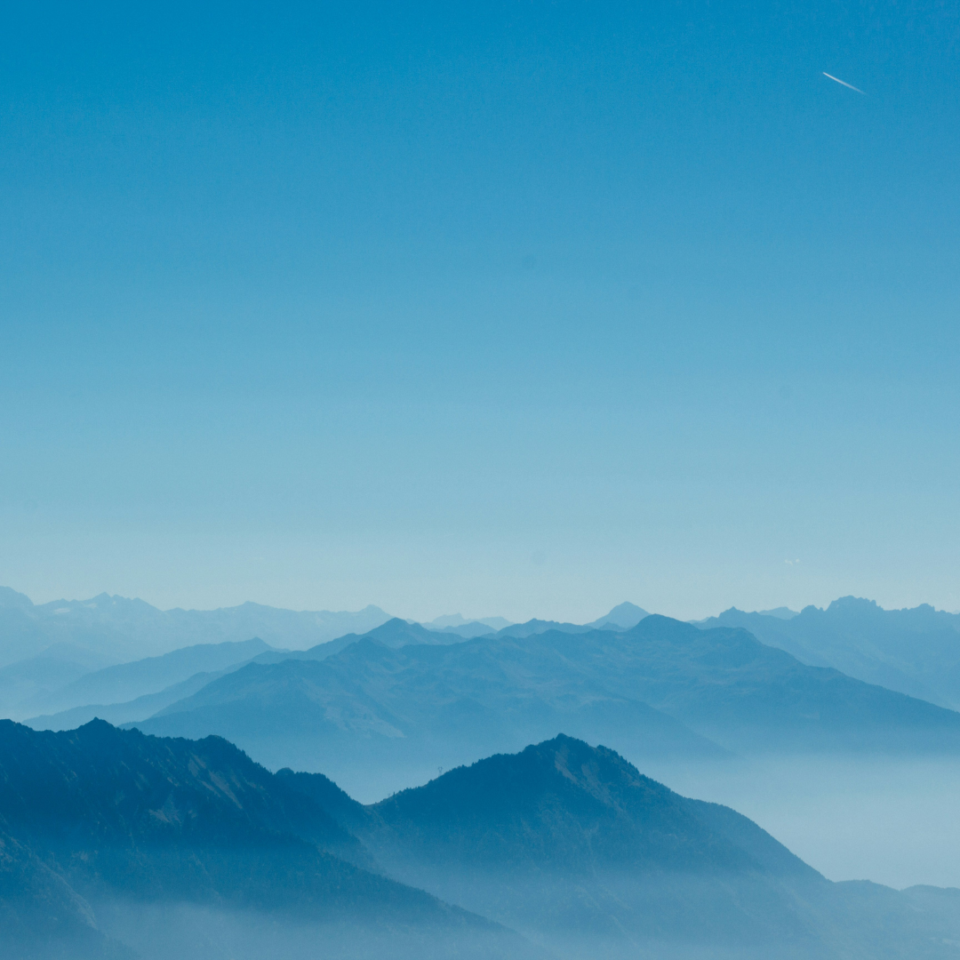 Paesaggio di montagne sfumate nel blu sotto un cielo azzurro limpido, simbolo di calma, introspezione e spiritualità.