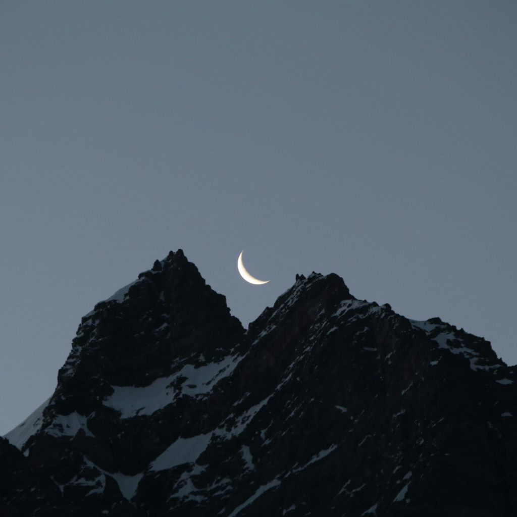 Luna crescente tra due montagne scure al crepuscolo, simbolo di mistero, interiorità e significato spirituale del colore nero.