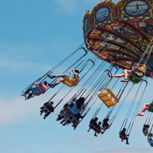 Persone su una giostra volante sospesa nel cielo blu, simbolo di libertà, leggerezza e felicità condivisa.